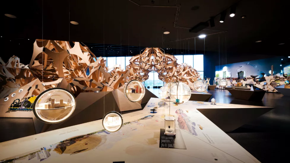 Der Denkraum Natur mit einer großen Holzskulptur im Hintergrund. Im Vordergrund baumeln Glaskugeln mit kleinen Modellen von Städten