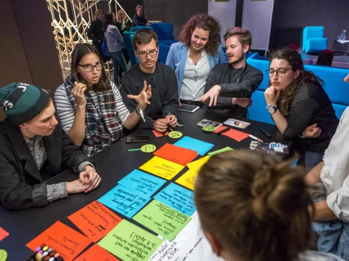 Menschen diskutieren an einem Tisch. Vor ihnen liegen Karteikarten.